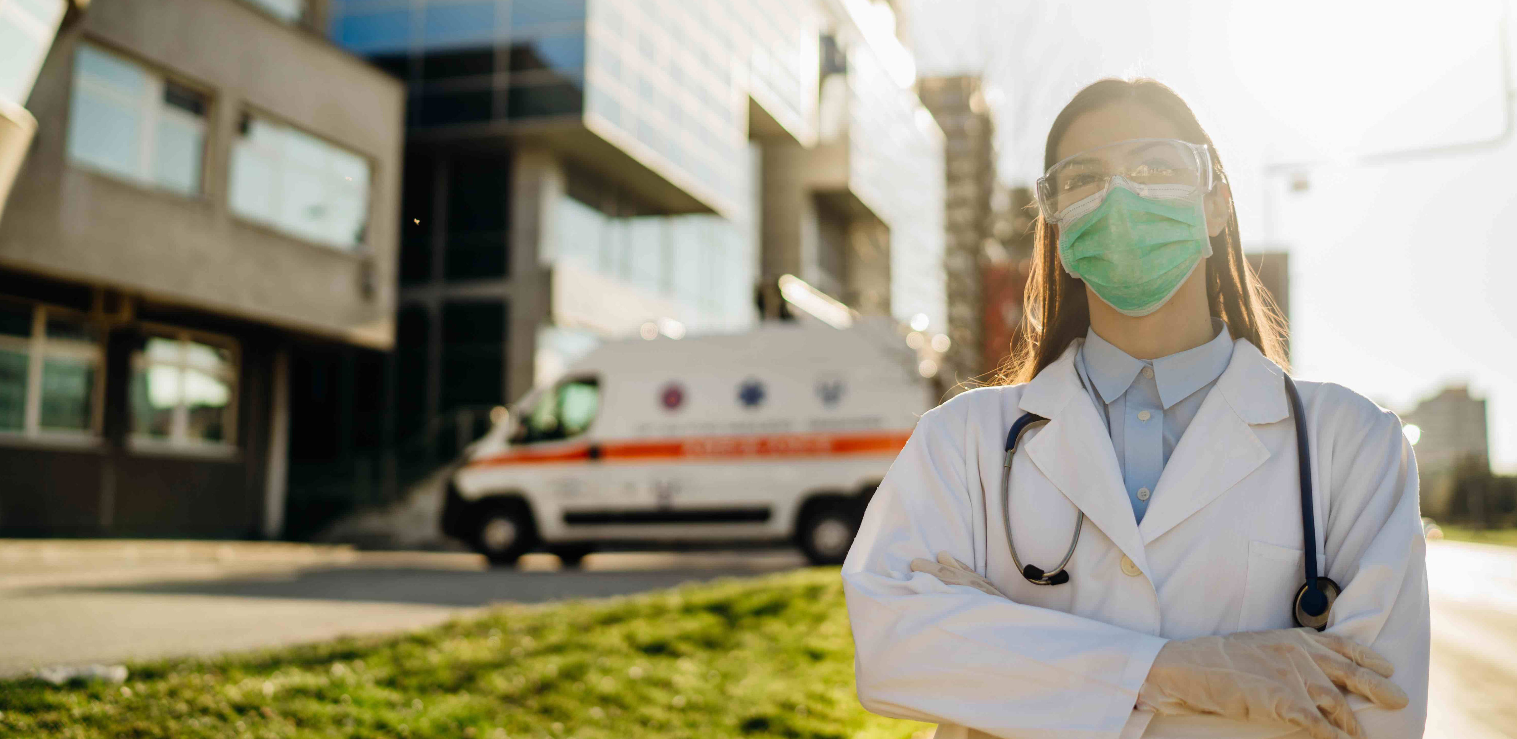 A provider with a mask standing in front of a hospital