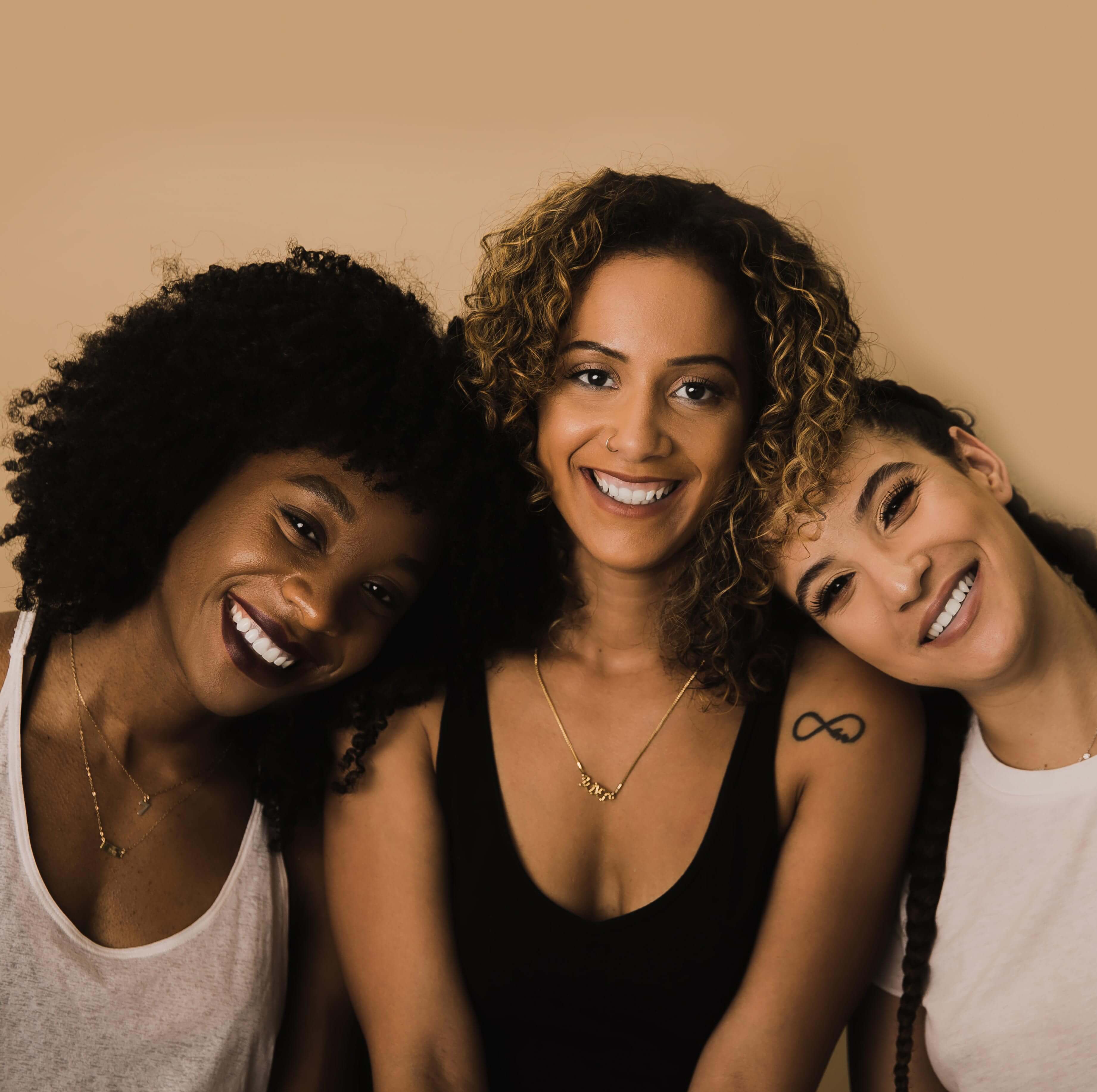 Three black and brown women smiling into the camera