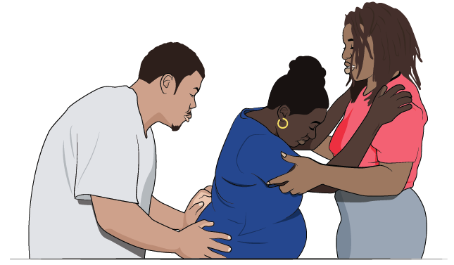 Pregnant woman in labor holding on to her doula with her male partner supporting her