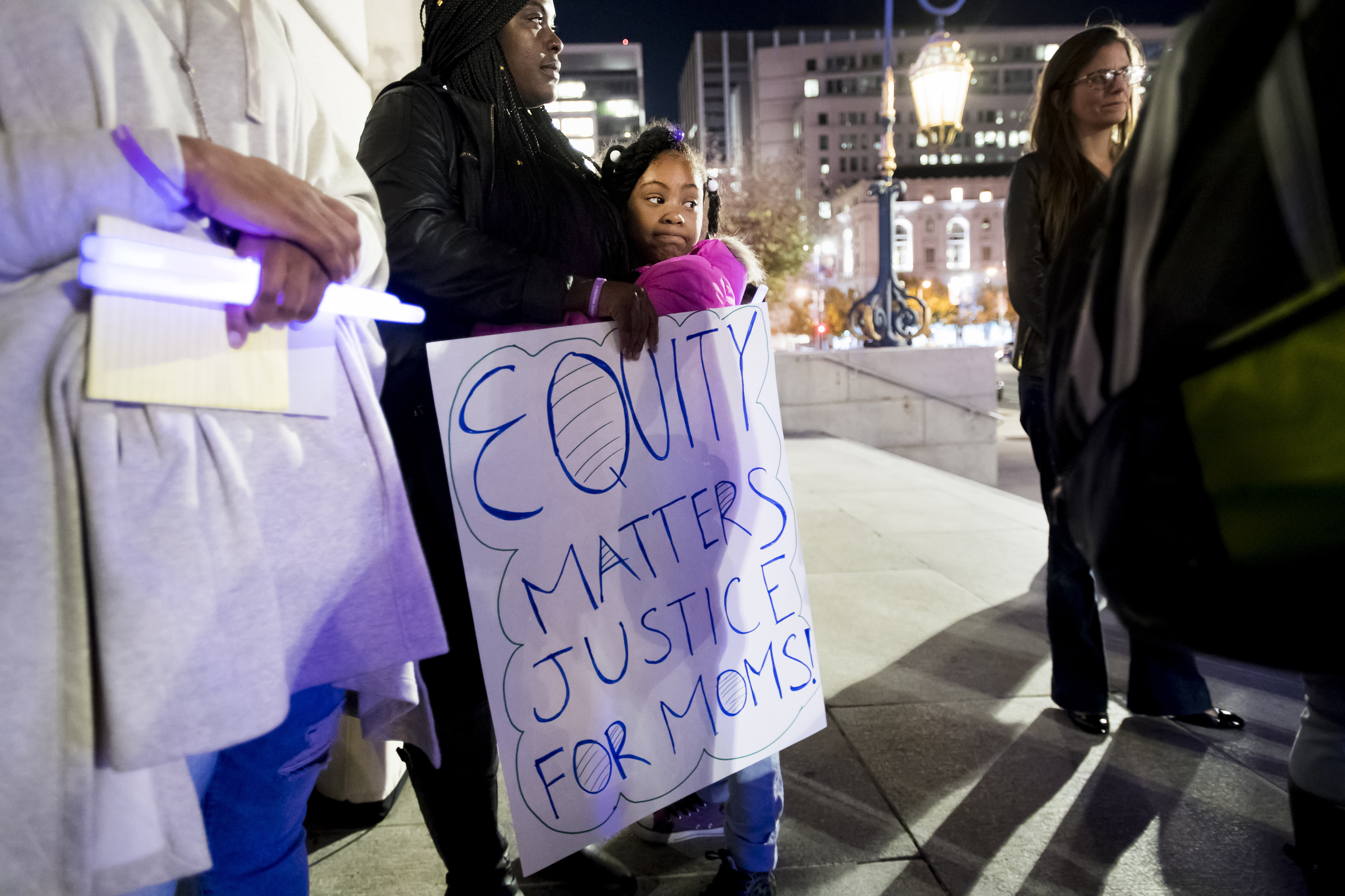 a mother and child holding an, "equity matters justice for moms" sign at the symposium rally